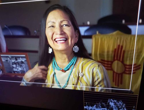 Woman in Native American earrings, necklace and shirt smiles